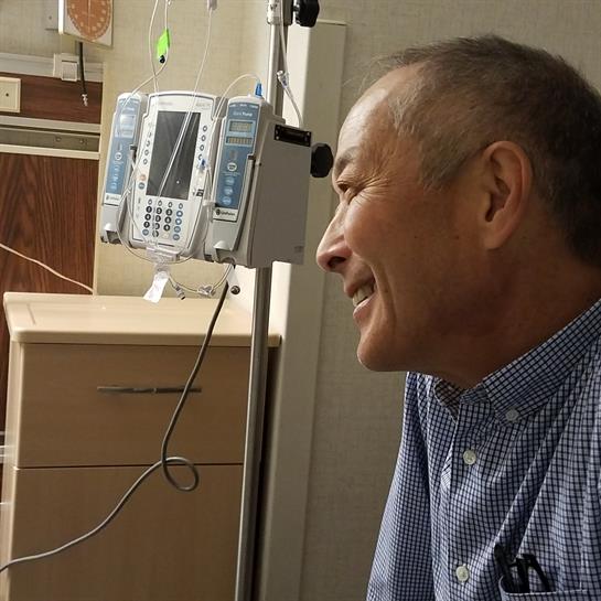 A man smiles warmly while interacting with a family member in a hospital setting.
