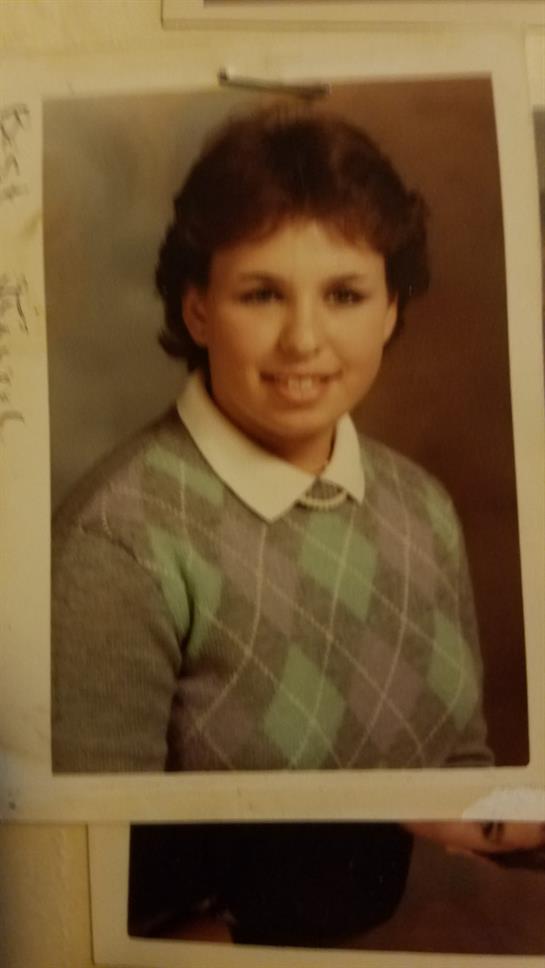 A person poses for a studio portrait, wearing a sweater and smiling at the camera.