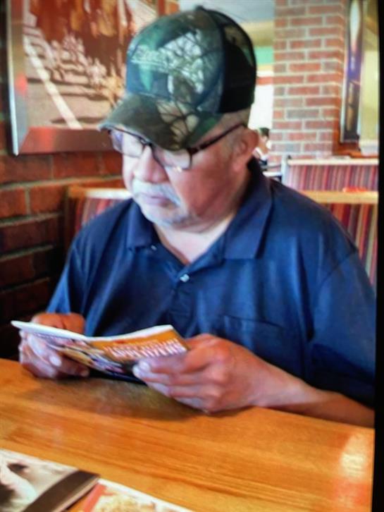 An elderly man examines a menu while sitting at a wooden table in a restaurant, enjoying his time.