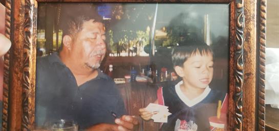 Grandfather smiles as he engages with his grandson at a family event in a lush outdoor setting.