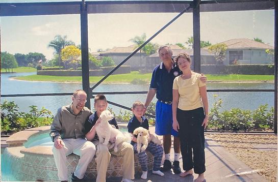 Family members pose happily by the water with their dogs on a bright sunny afternoon.