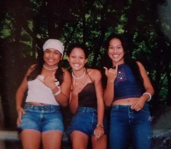 Three young women stand together outdoors, smiling and posing playfully in summer attire.