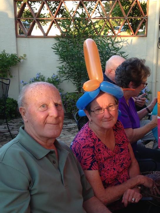 Elderly couple has fun at a cheerful gathering with colorful balloon hats in a garden.