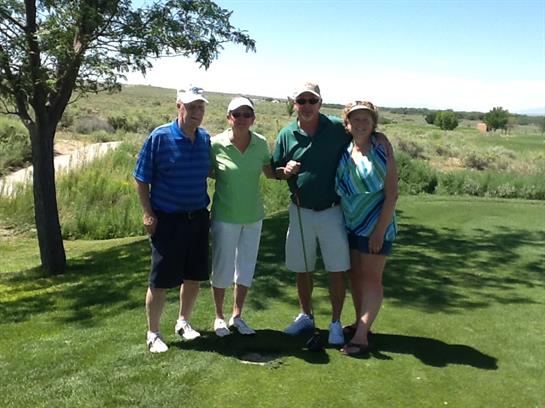 Four friends smile while posing together on the golf course under a clear blue sky.