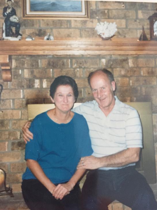 A cheerful elderly couple sits closely together, smiling warmly in their inviting living room.