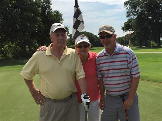 Three friends gather on a golf course under sunny skies, celebrating a successful round of golf.