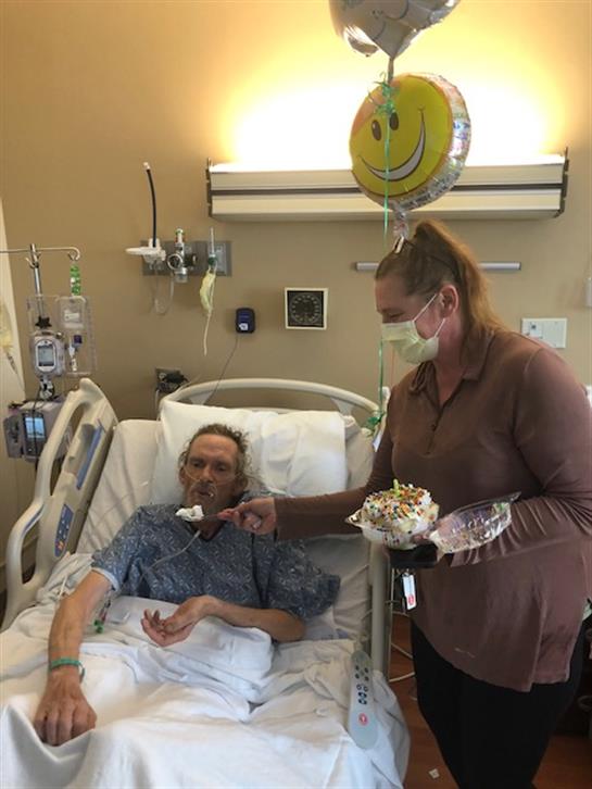 A hospital room filled with warmth as a woman feeds a man dessert while holding a balloon.