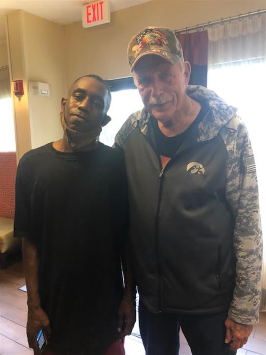 Two men stand close, smiling with a warm atmosphere in a casual indoor location.