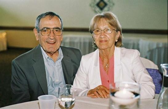 Elderly couple shares smiles and conversation at a family gathering in a warmly decorated space.