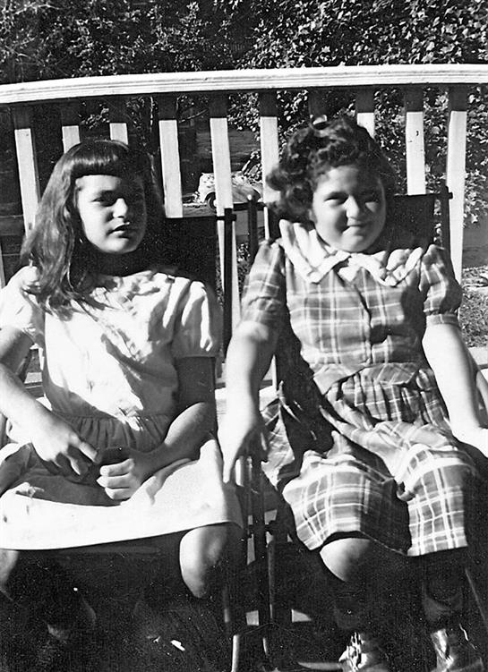 Two girls sit on a porch enjoying a sunny day.