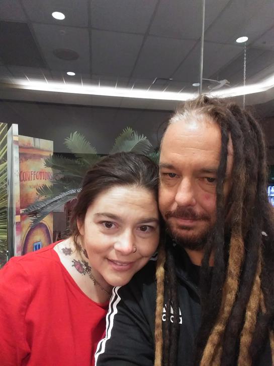 A couple embraces closely, sharing smiles in a vibrant location filled with nightlife energy.