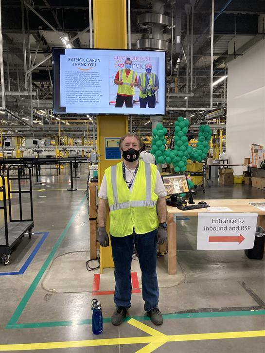 A worker in safety gear is positioned at the entrance of a large warehouse, overseeing operations.