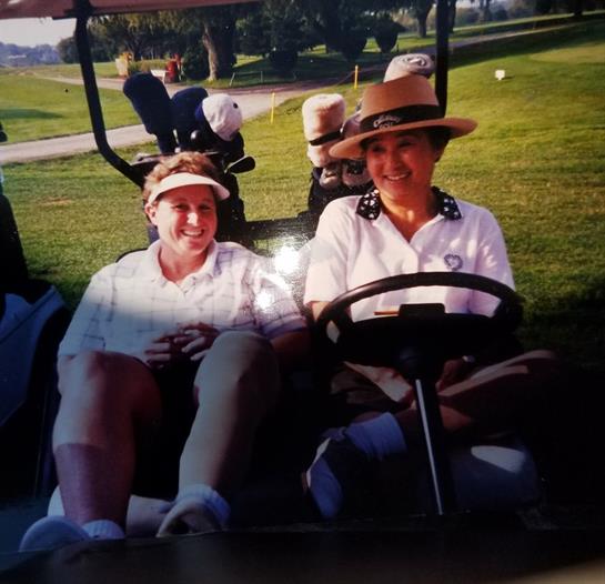 Women smile and pose for a photo on a golf cart, enjoying a sunny day on the course.