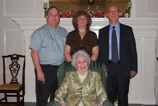 Four family members gather around the matriarch, celebrating together in a warm living room.