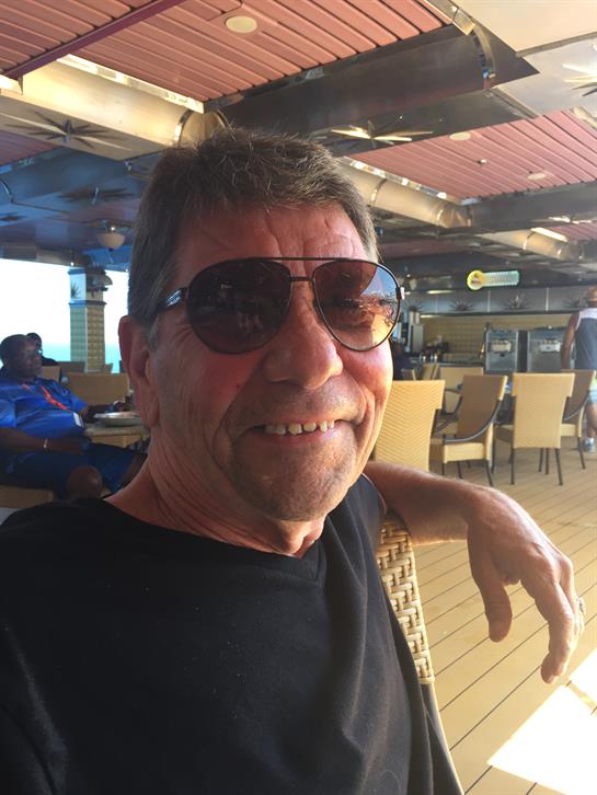 Older man relaxes at an outdoor restaurant, smiling and enjoying the warm, sunny atmosphere.