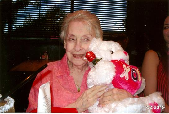 Elderly woman smiles while cuddling a plush bear, embracing joy indoors.