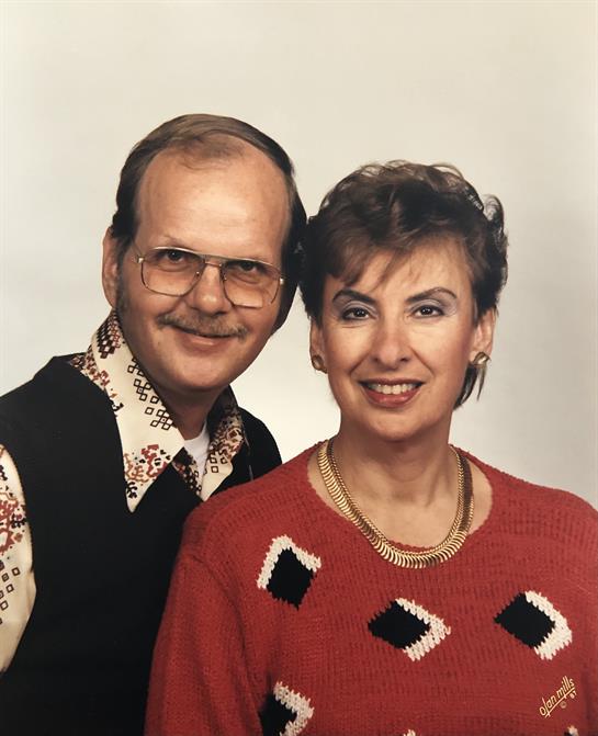 A man and woman smile brightly, dressed in colorful vintage outfits, creating a joyful atmosphere.