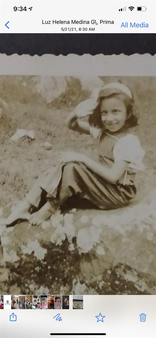 Girl with a playful smile sits on a rock in a grassy area, enjoying a sunny day outside.