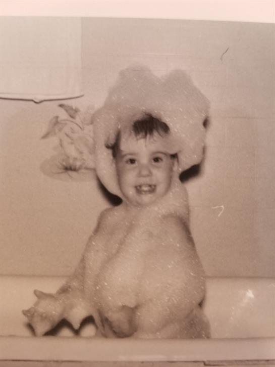 A cheerful young child sits in a bathtub, wearing a towel and a bathing cap, enjoying bathtime.
