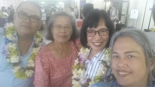 Group of friends joyfully posing together with floral leis at an bustling airport in Hawaii.