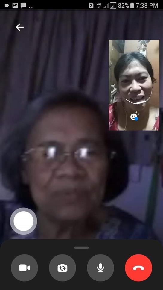 An elderly woman smiles while video chatting with a younger woman on a digital device at home.
