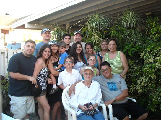 Family members of different ages pose together outdoors, smiling in a lush garden setting.