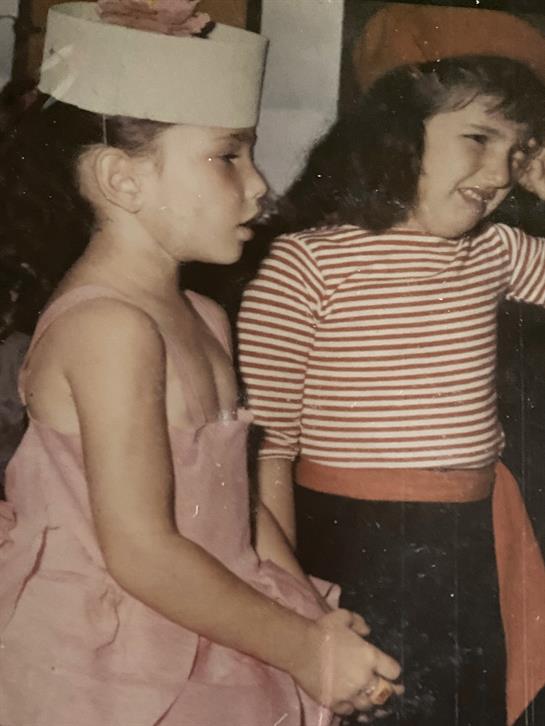 Two girls are engaged in a cheerful moment at a festive gathering wearing colorful costumes.