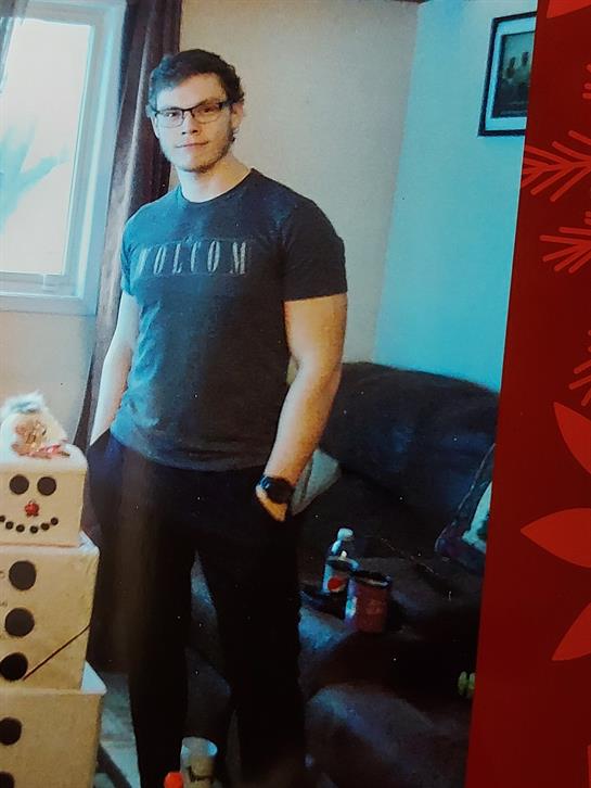 A young man stands beside a snowman in a cozy, holiday-decorated living room.