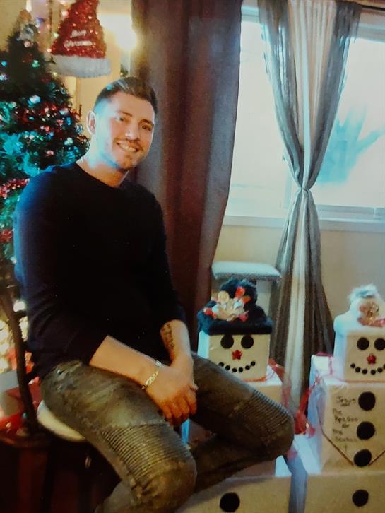 A cheerful man sits comfortably next to a decorated Christmas tree and festive snowmen.