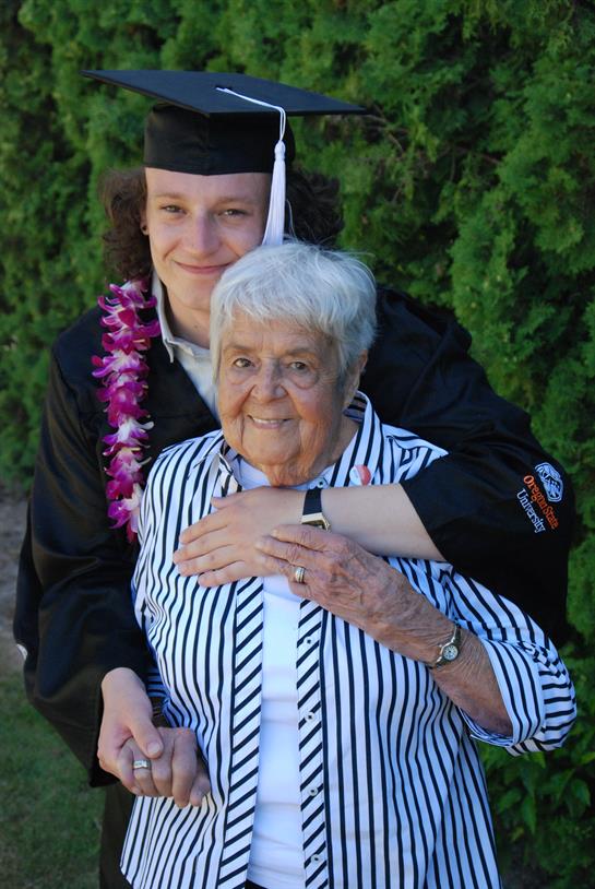 A joyful graduate in a cap and gown poses with their grandmother, showcasing love and pride.