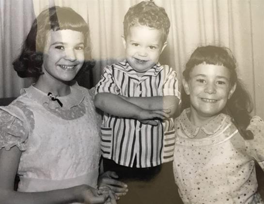 Three young children, two girls and a boy, smile joyfully while standing in a retro room.