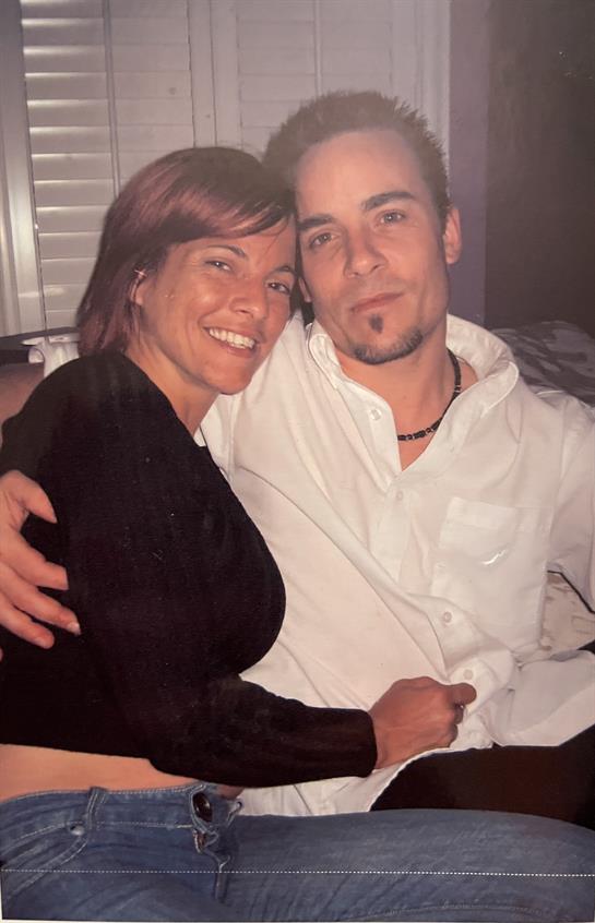 A couple sits closely on a couch, smiling and sharing a cozy moment together at night.