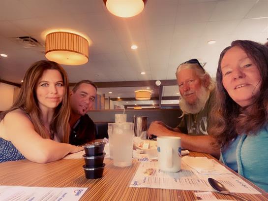 Group of four friends sharing a meal and smiles in a relaxed dining environment.