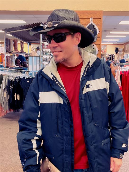 A man in a cowboy hat and sunglasses browses winter apparel in a retail store.