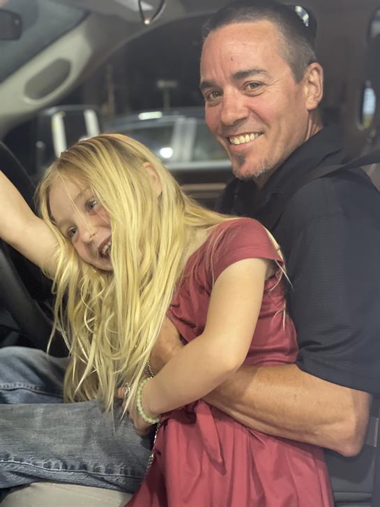 A smiling father holds his daughter in a car, both enjoying a fun and playful time together.