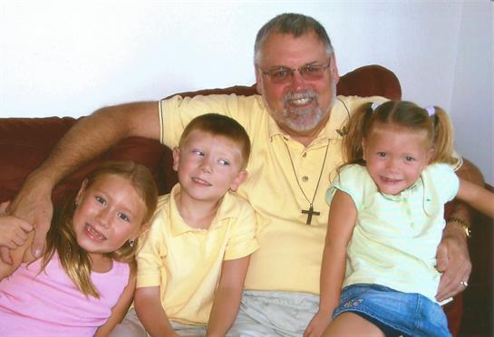 Grandfather sits on a couch with three smiling grandchildren, creating lasting family memories.