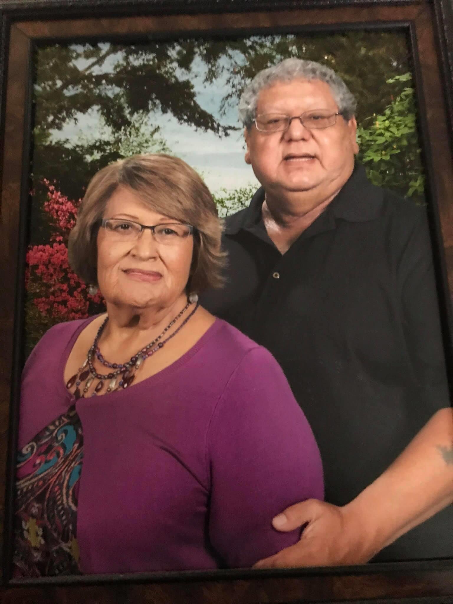 A couple stands closely together, smiling gently in a garden filled with greenery and flowers.