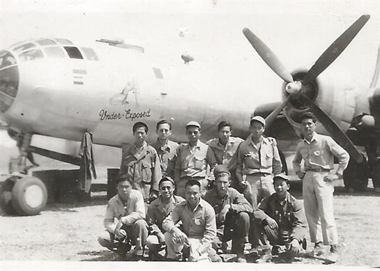 Soldiers stand together in military uniforms before a large aircraft at a base in the Pacific.