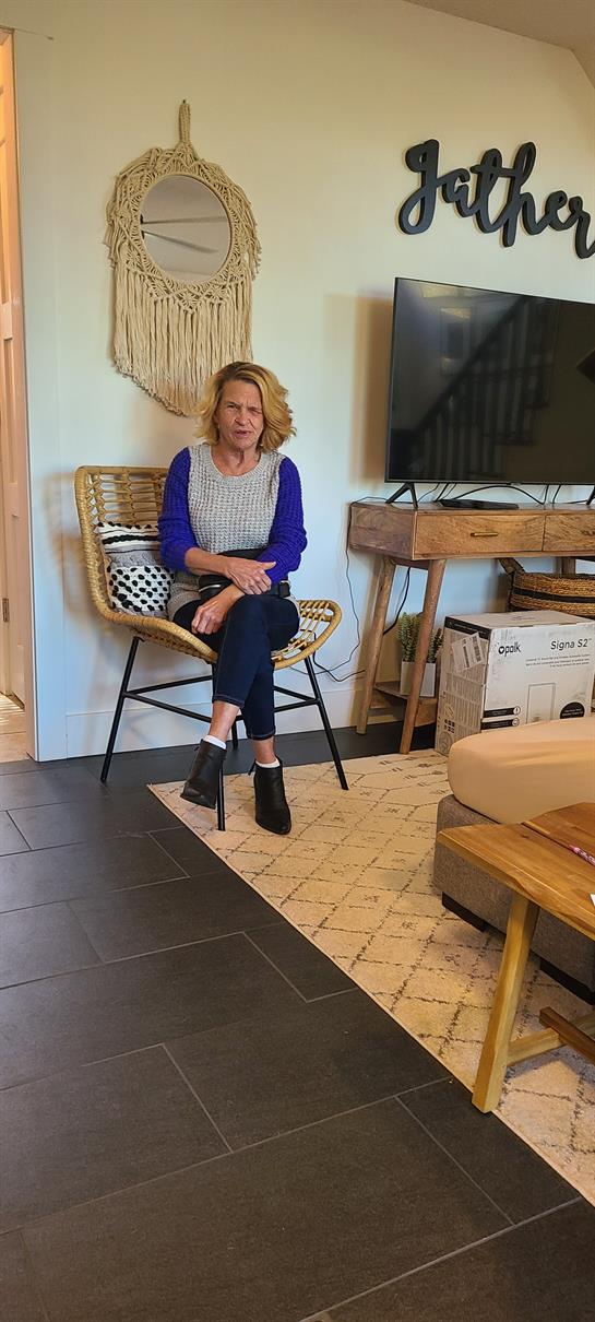 A woman rests on a chair in a contemporary living room filled with natural light and stylish decor.