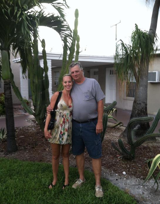 A couple stands together in a tropical garden, smiling and enjoying the evening atmosphere.