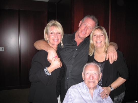Four adults enjoy each other's company, smiling and embracing in a dimly lit space.