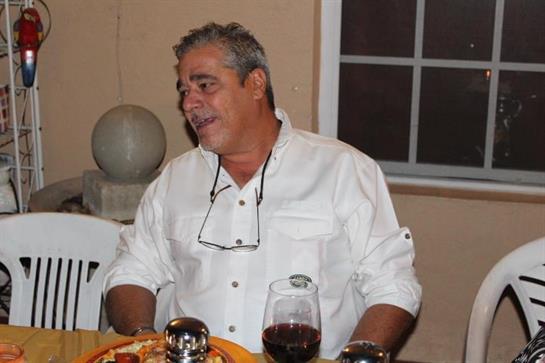 A man laughs while seated at a table filled with food and drinks, sharing a joyful moment.