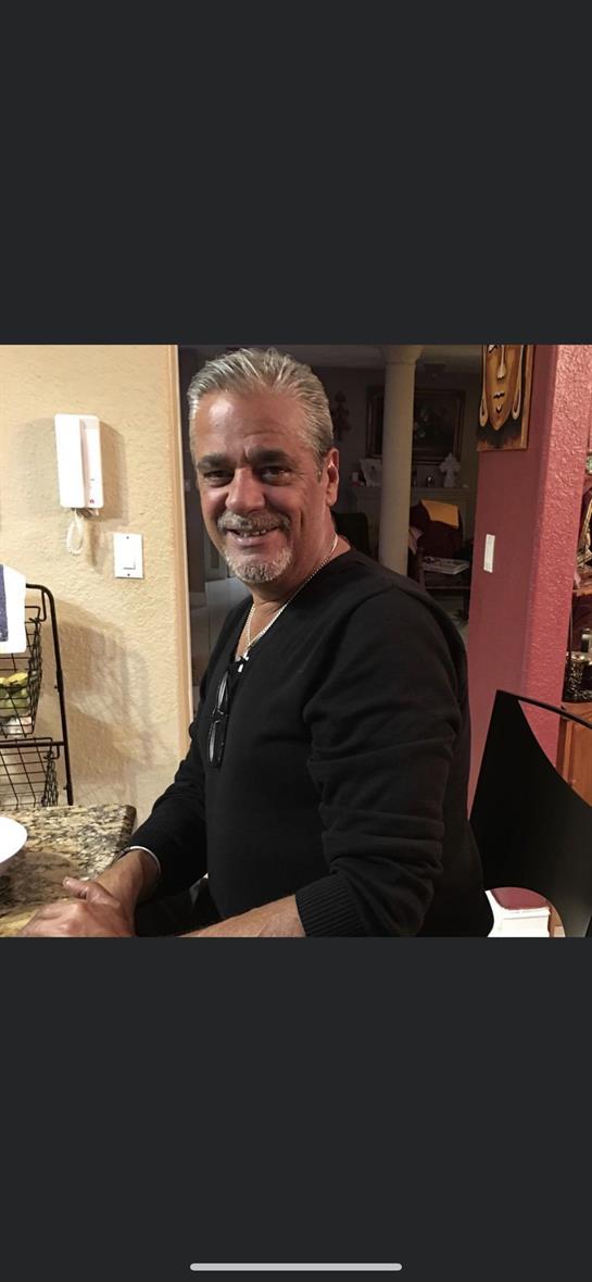 A smiling man enjoys cooking in a warm kitchen while gathering with friends during the evening.