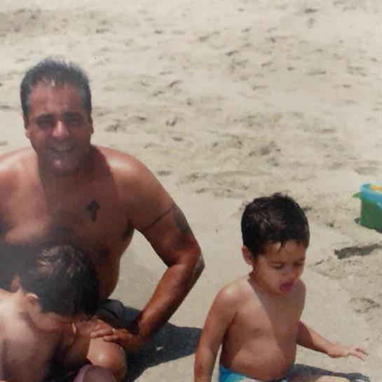 A father plays with his two young children on a sandy beach under bright sunlight.