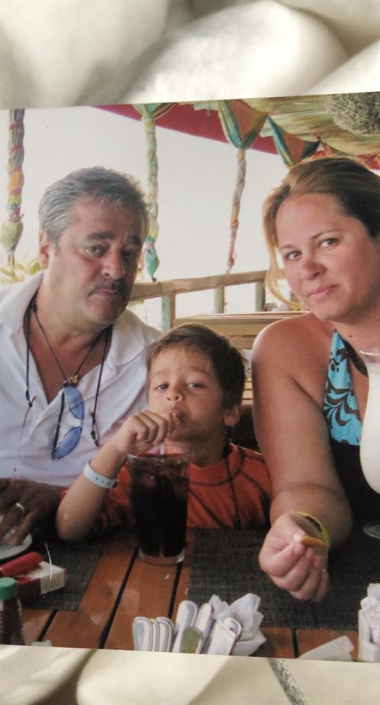 Family gathers around a table at a beachfront restaurant, sipping drinks and smiling together.
