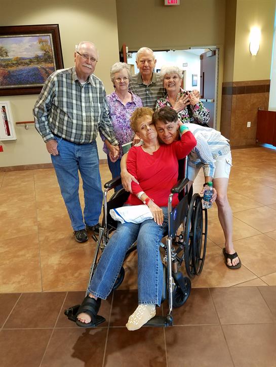 A happy family of six poses with a smiling elderly woman in a wheelchair at a community center.
