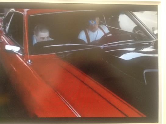 Two individuals enjoy a drive in a classic red car on a bright sunny day.