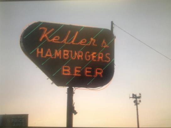 Bright neon sign advertising hamburgers and beer at twilight in a bustling area.