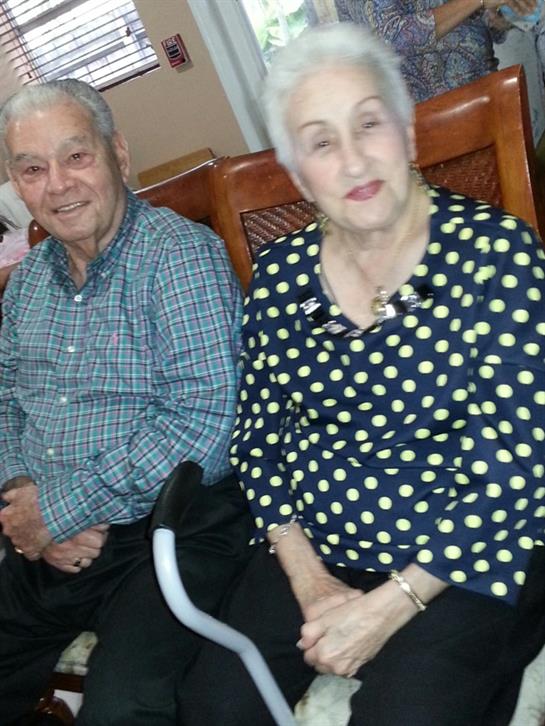 Older adults share smiles and warmth at a gathering in a cheerful, indoor space.