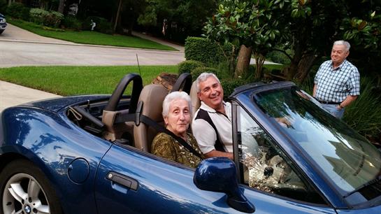 Elderly pair smiles while sitting together in a convertible parked on a quiet street.